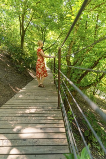 A woman on a wooden footbridge in the forest, surrounded by green trees, Botanical Garden, The