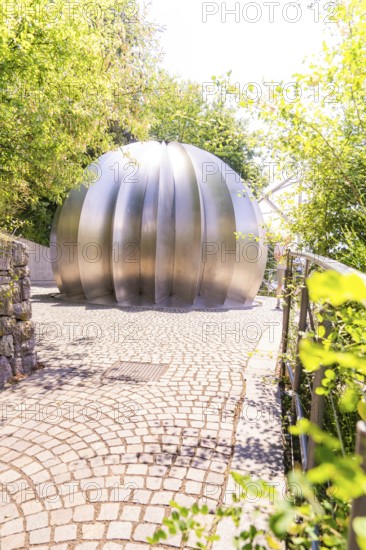 Modern metal sculpture in a sunny park with green foliage in the background, Botanical Garden, The