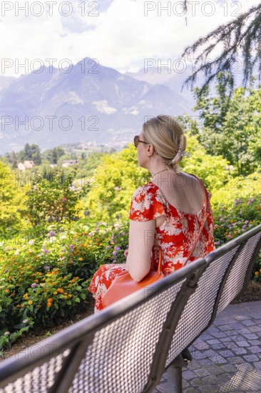 Woman in a red dress sitting on a bench and enjoying the view of the mountains, Botanical Garden,