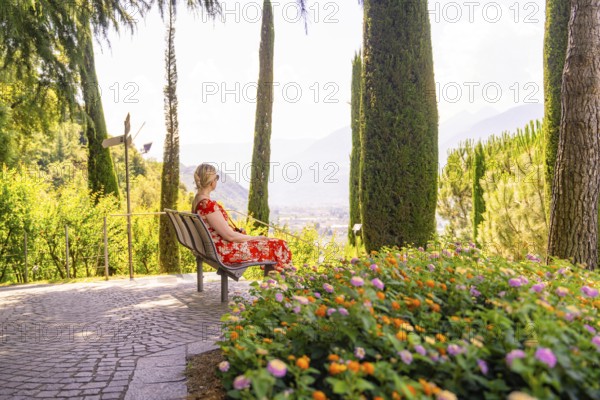Woman in a red dress sitting on a bench overlooking a scenic view, Botanical Garden, The Gardens of