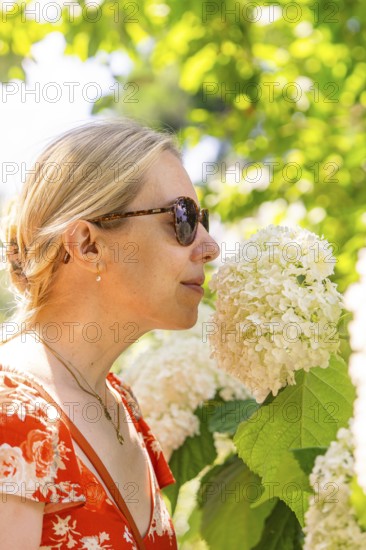 Woman smelling a white flower, surrounded by green plants, wearing a red dress, Botanical Garden,
