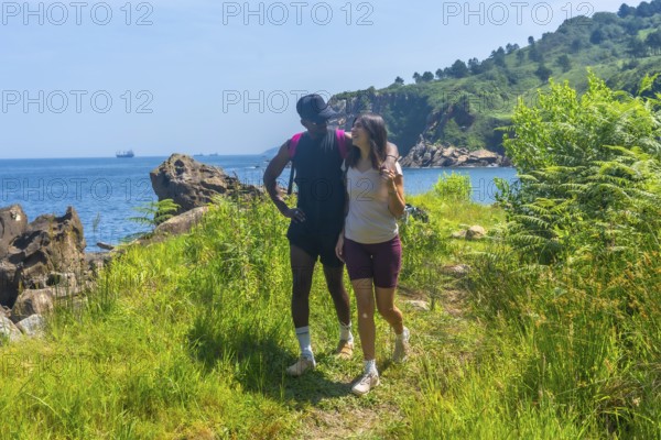 Interracial couple walking along a coastal path, enjoying the scenic views of the ocean and green