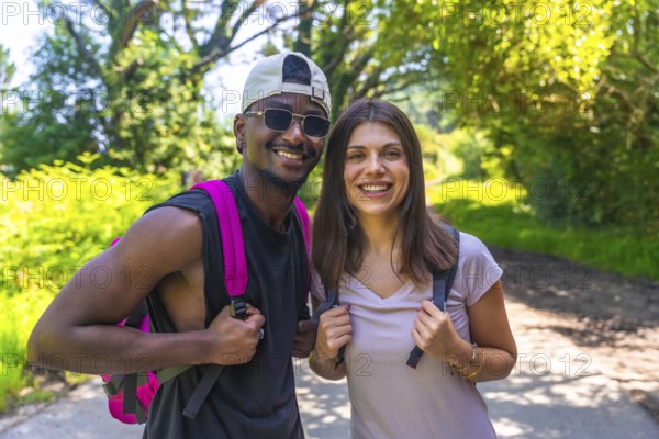 Hikers wearing backpacks are smiling joyfully while trekking along a forest path, enjoying the