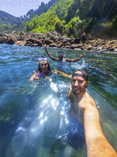 Three friends enjoy snorkeling in the refreshing ocean water, capturing a selfie moment amidst a