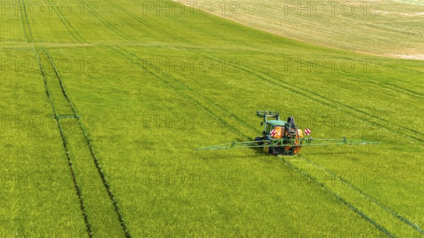 Farmer with tractor working in the field. In early summer, he fertilises the grain for an optimum