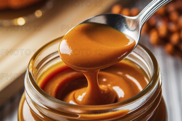 Close-up of silver spoon scooping rich pumpkin butter from glass jar. Warm autumn kitchen scene