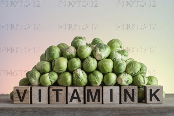 Brussels sprouts stacked on wood with blocks spelling Vitamin K. Rustic studio scene highlighting
