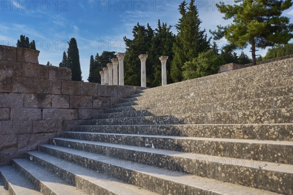 Stone staircase with old columns, framed by trees under a blue sky, open staircase to the second