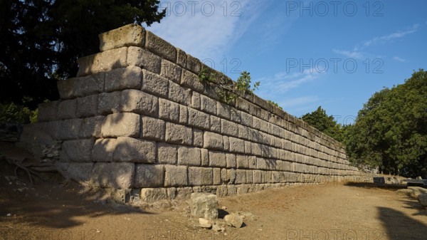 Stone wall in a natural setting with clear blue sky, Wall Upper Terrace, Asklipion, Asklepieion,