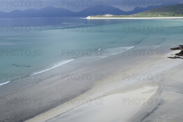 Gentle waves roll over fine sand against a majestic backdrop of mountains and calm sea, Seilebost