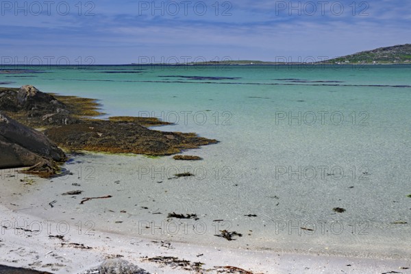 Tranquil beach landscape with rocks, sea and clear blue sky with seaweed on the shore, Eriksay,