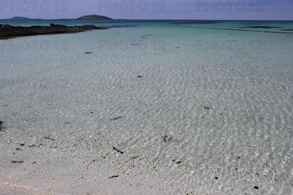 Crystal clear turquoise water on a sandy beach with islands on the horizon under a blue sky,