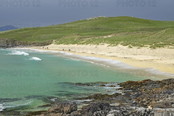 Picturesque coastal landscape with green hill, sandy beach and turquoise sea under a cloudy sky,