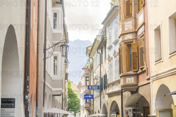 Narrow alley in the old town centre with classic buildings and shutters, mountains in the
