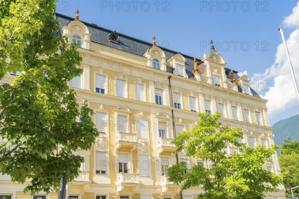 Classic building with elegant façade flanked by green trees under a blue sky on a sunny day,