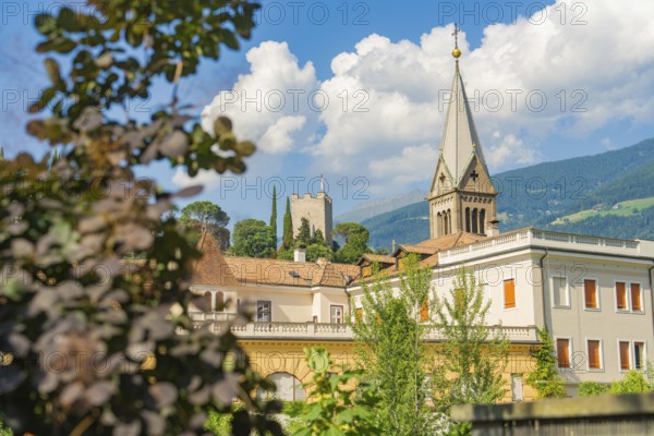 Historic building with church tower and picturesque mountains in the background under a cloudy sky,