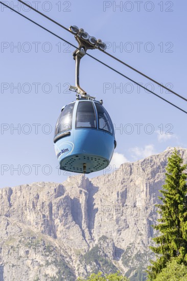 Blue cable car gondola floating in front of an impressive mountain range under a clear sky, Alpe di