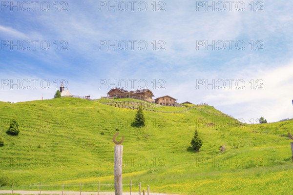 Wooden building on a green hill in front of a blue sky with white clouds, Alpe di Siusi, Dolomites,