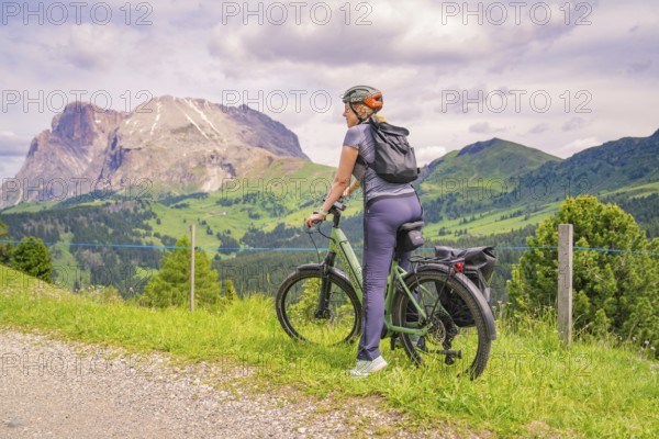 Cyclist on a path with a view of a mountain landscape under a cloudy sky, Alpe di Siusi, Dolomites,