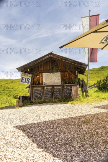 Wooden hut as an ice cream stand in a meadow in the mountains in the sunshine with flags and