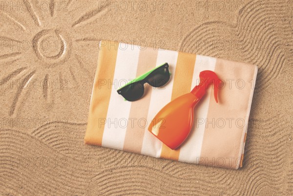 Drawing on the sand, sun and waves, sunglasses, with an orange bottle, beach towel, sun spray, on