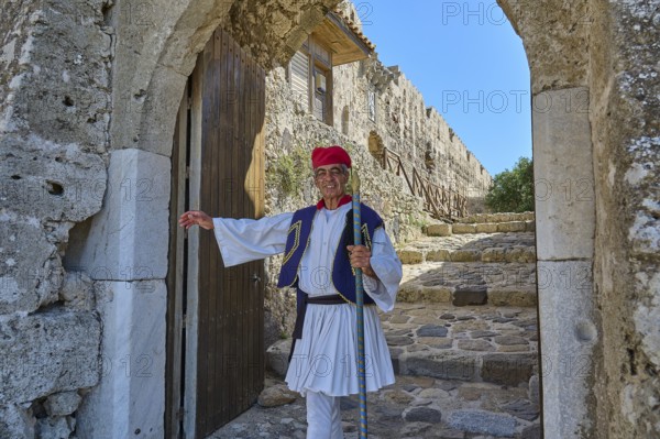 Man in traditional traditional costume kindly standing in front of historic archway, Antimacheia,