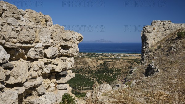 View through ancient ruins to a rocky landscape with the sea in the background, Kardamina,