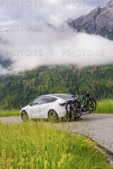 White car with bicycles on road, surrounded by misty mountain landscape and green forest, electric