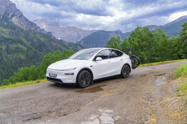 White car with bicycles on a winding mountain road, surrounded by dense greenery and cloudy sky,