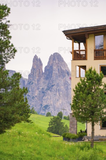 View of impressive rock formations behind a building with green foreground, Alpe di Siusi, South