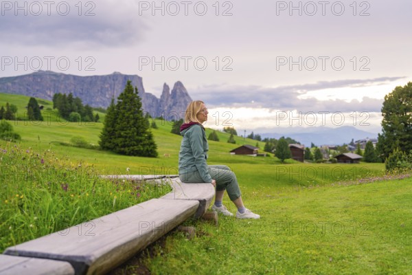 Woman enjoying the view in a green hilly landscape with mountains and clouds, Alpe di Siusi, South