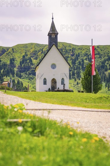 White church stands idyllically on a green meadow with mountain backdrop and flag, Alpe di Siusi,