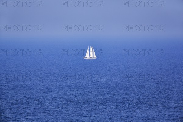 Blue sea, calm water surface, single sailing boat on the horizon, haze, offshore island Helgoland,