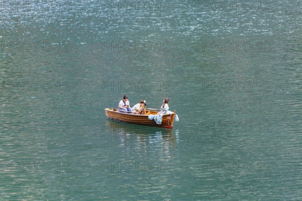 Three people in a small wooden boat on a quiet lake enjoying a relaxing trip, Lake Braies, South