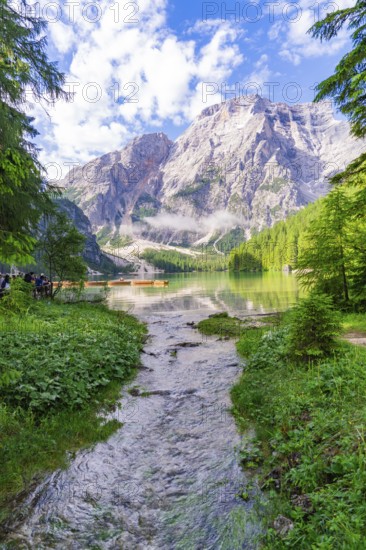 A clear mountain lake surrounded by impressive mountains and dense forest under a partly cloudy