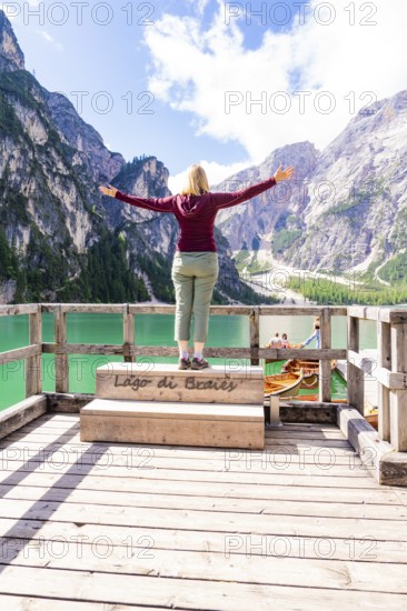 A woman stands with outstretched arms on a balcony and enjoys the view of mountains and a green