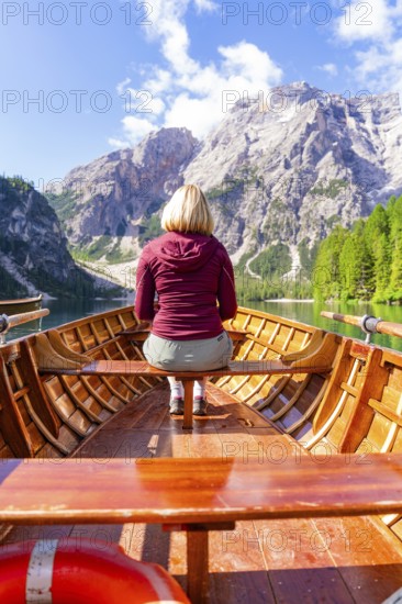 Back view of a woman in a boat on a mountain lake in sunny surroundings, Pragser Wildsee, South