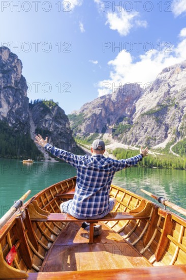 Man spreads his arms with joy on a boat on a mountain lake, Pragser Wildsee, South Tyrol,