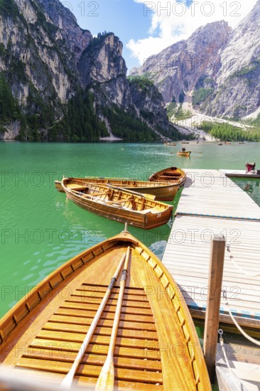 Several wooden boats are moored to a jetty on a calm, emerald-green mountain lake, Lake Braies,