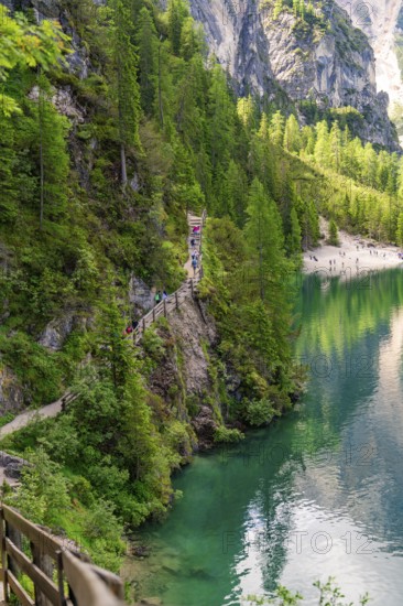 A narrow path winds along a steep slope with a view of an emerald green lake, Pragser Wildsee,