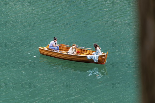 Three people in a wooden boat, floating relaxed on the water, in peaceful surroundings, Lake