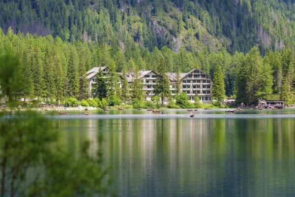 A hotel on the lake shore with surrounding trees and mountains, quiet atmosphere, Lake Braies,