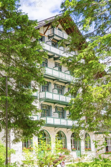 A white hotel building with balconies surrounded by green trees, Lake Braies, South Tyrol,