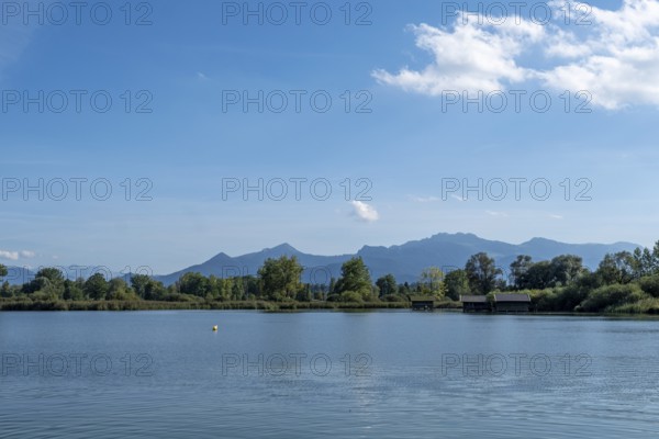Tranquil lake with views of wooded shores and mountain landscape under a clear blue sky, Chiemsee,