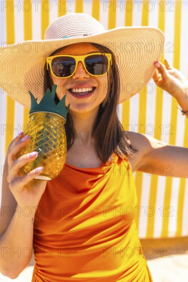 Happy woman wearing a straw hat and sunglasses holding a pineapple shaped cocktail in front of
