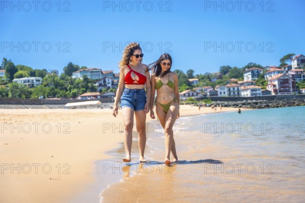 Two friends enjoying a sunny beach day, walking along the shore, laughing and soaking up the