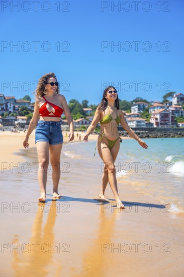 Two friends enjoying a sunny beach day, walking along the shore, laughing, and creating joyful