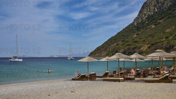 Kamari beach, summer beach scenery with deckchairs and parasols, two sailing boats in the calm blue