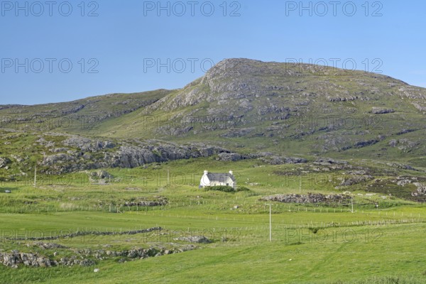 Small house in a green valley surrounded by mountains under clear skies, Isle of Barra, Hebrides,