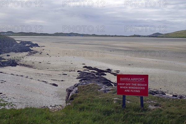 Empty beach with a warning sign in the foreground, surrounded by dunes and a wide sky, airport,